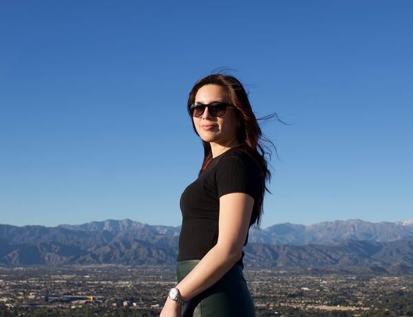 Camila in mid-length photo wearing sunglasses in front of blue sky and mountains