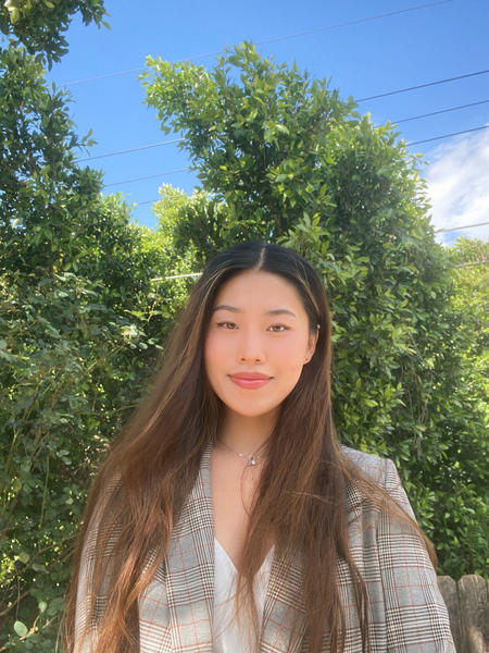 Judy from mid-torso up, smiling in front of a row of trees