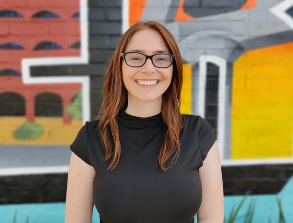 Middle distance photo of Kyla smiling at the camera in front of colorful backdrop