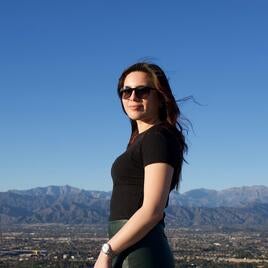 Camila in mid-length photo wearing sunglasses in front of blue sky and mountains